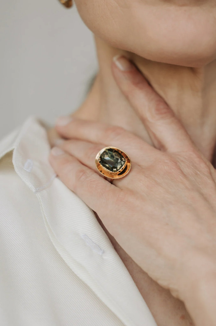 Gold ring with a dark faceted center stone worn on a hand.